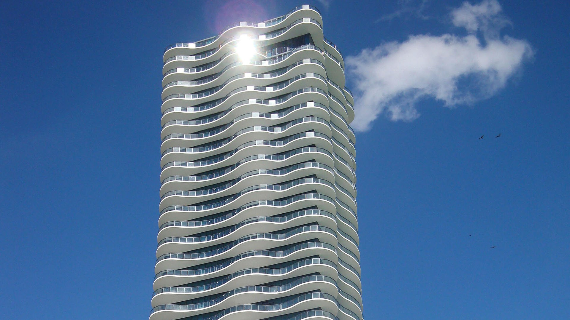 Sunlit tower closeup at Regalia in Sunny Isles Beach showing the sculpted curved balconies and glass facade of luxury and ultra luxury condos.