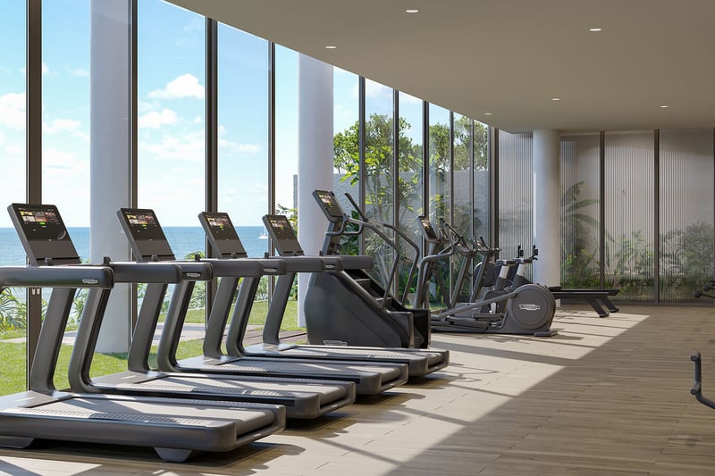 Oceanfront fitness center at Rosewood Residences Hillsboro Beach, Florida with treadmills and cardio equipment by floor-to-ceiling windows overlooking the Atlantic, luxury and ultra luxury preconstruction condos.