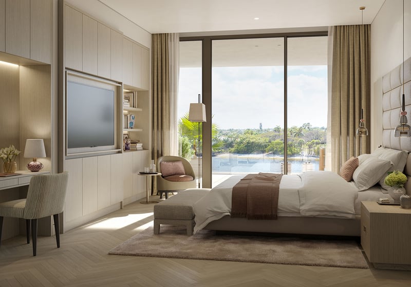 Rosewood Residences Hillsboro Beach, Florida primary bedroom suite with king bed, built-in TV wall, work desk and floor-to-ceiling glass opening to balcony water views, showcasing luxury and ultra luxury preconstruction condos.