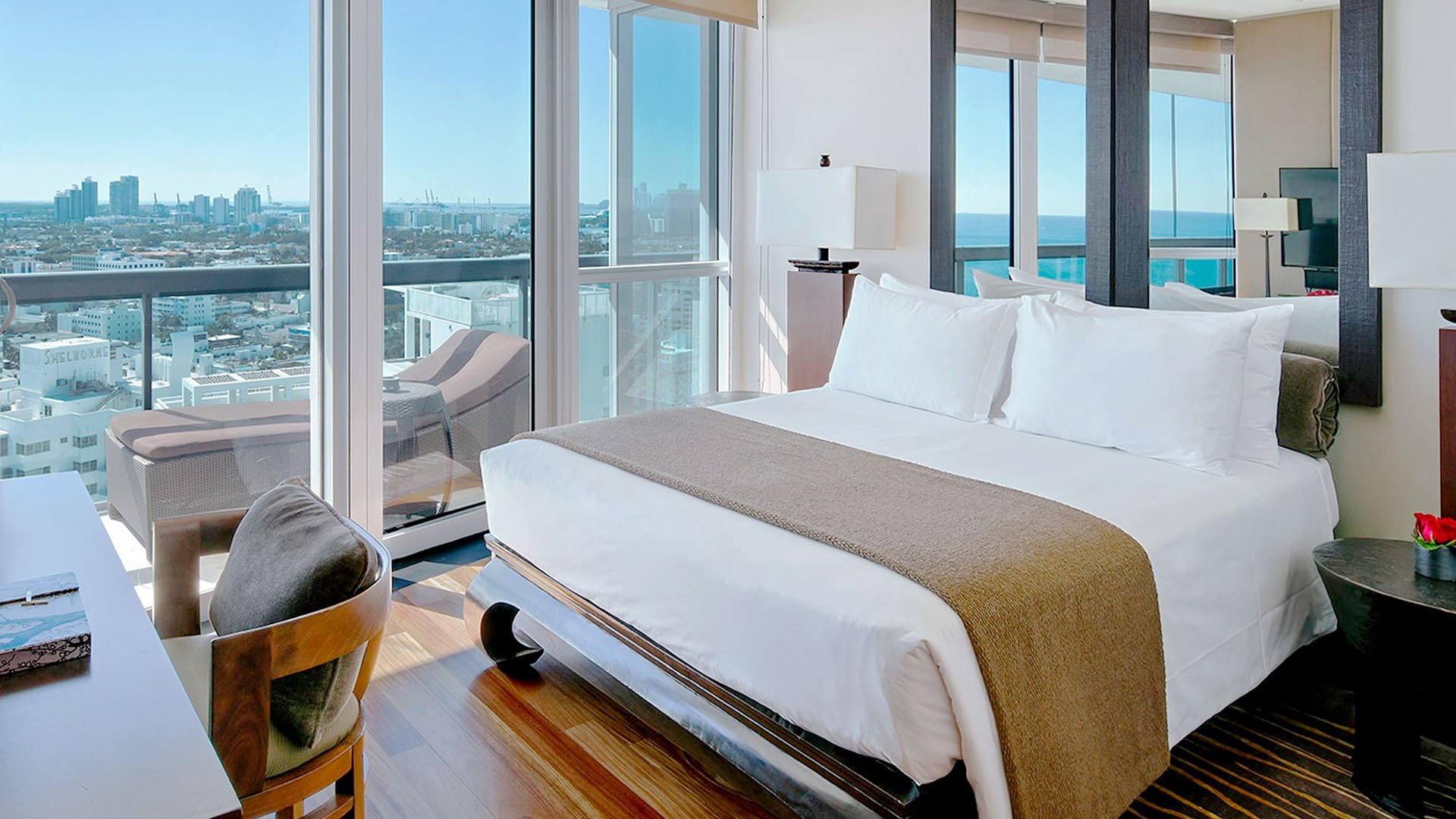 Corner bedroom at Setai Miami Beach in Miami Beach showcasing luxury and ultra luxury condos with floor-to-ceiling glass, a private balcony with loungers, and sweeping city and water views.