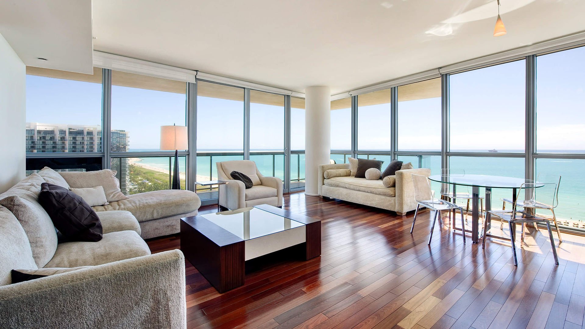 Corner living room at Setai Miami Beach in Miami Beach presenting luxury and ultra luxury condos with wraparound glass, warm wood floors, modern seating, and open ocean views.