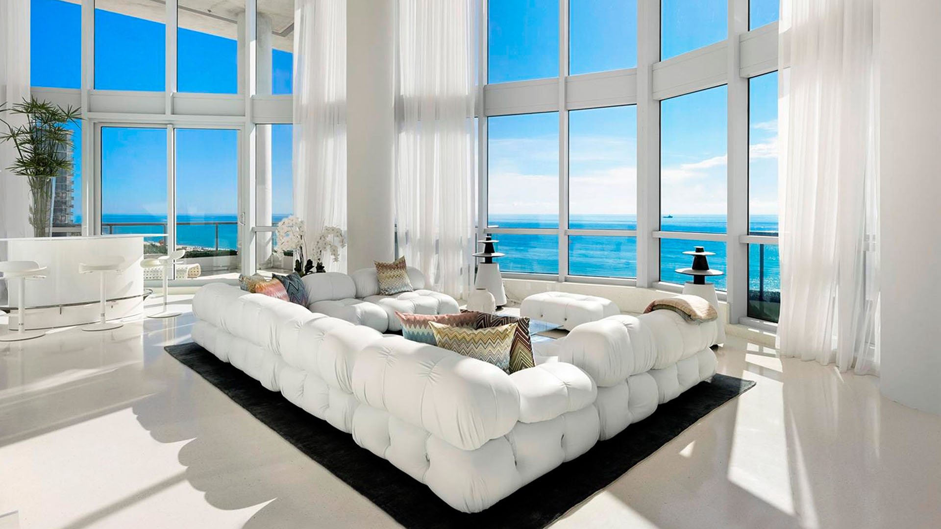 Double-height living room at Setai Miami Beach in Miami Beach highlighting luxury and ultra luxury condos with dramatic floor-to-ceiling windows, white tufted seating, and bright ocean views.