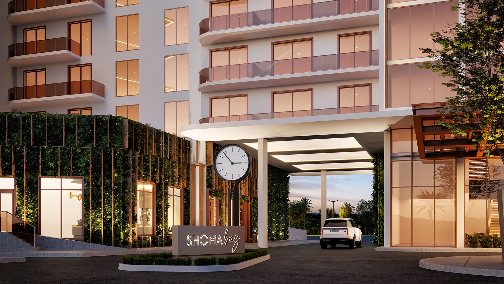 Shoma Bay North Bay Village, Miami, Florida porte-cochere entrance at dusk with illuminated driveway canopy, clock and branded signage, arriving to luxury and ultra luxury preconstruction condos in a mixed-use setting.
