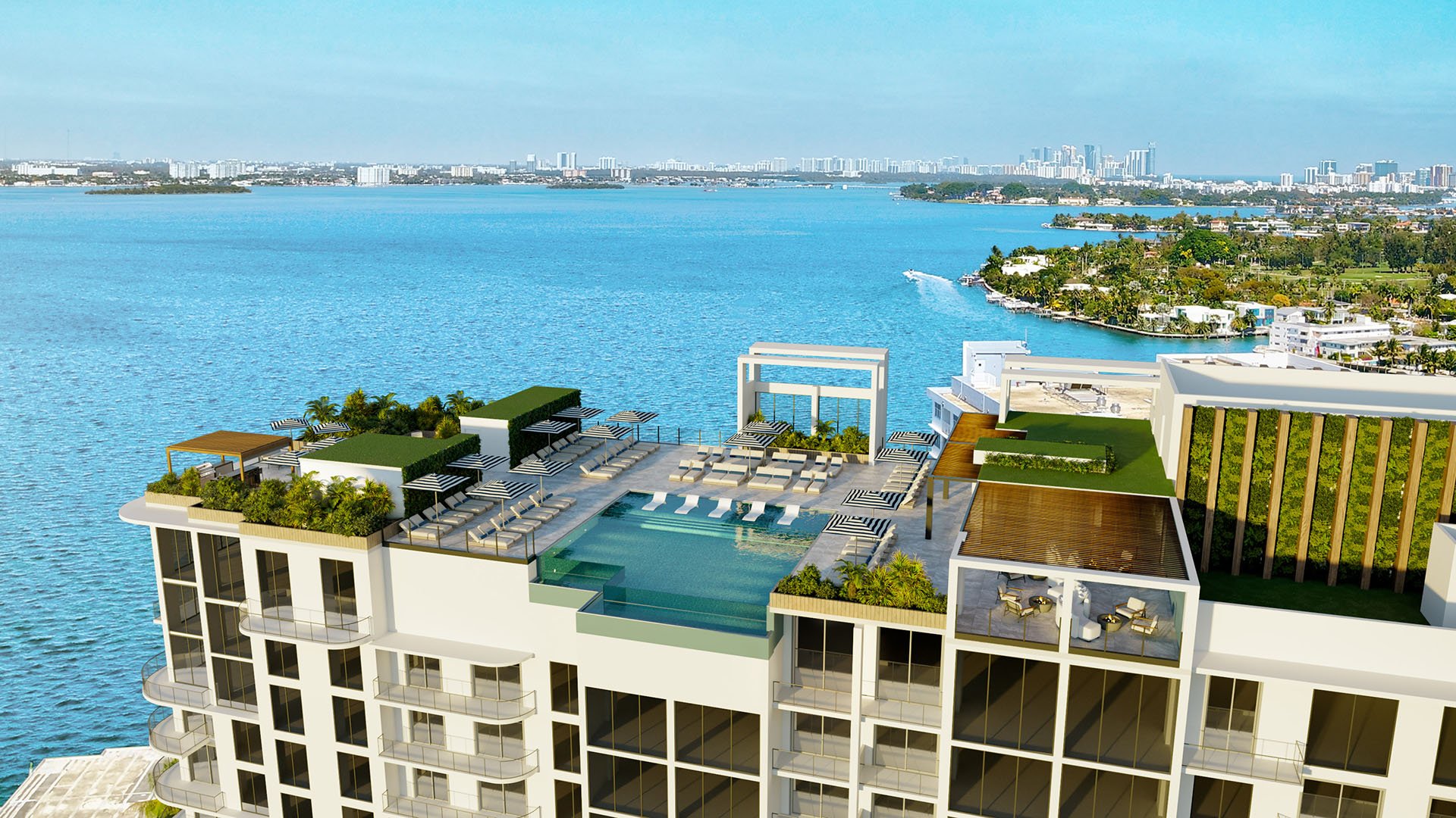 Aerial view of Shoma Bay North Bay Village rooftop pool deck with infinity pool, sun loungers, umbrellas and lush landscaping over Biscayne Bay, showcasing luxury and ultra luxury preconstruction condos in Miami, Florida.