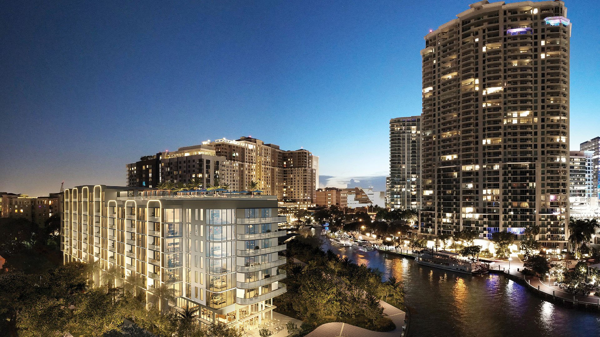 Aerial night rendering of Sixth and Rio in Fort Lauderdale, FL, showing riverfront setting, illuminated facade and city skyline - luxury and ultra luxury preconstruction condos by the water.