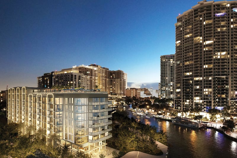 Aerial night rendering of Sixth and Rio in Fort Lauderdale, FL, showing riverfront setting, illuminated facade and city skyline - luxury and ultra luxury preconstruction condos by the water.