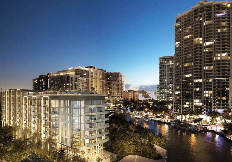 Aerial night rendering of Sixth and Rio in Fort Lauderdale, FL, showing riverfront setting, illuminated facade and city skyline - luxury and ultra luxury preconstruction condos by the water.