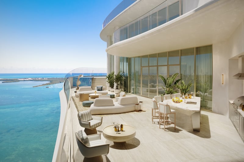 Curved waterfront penthouse terrace with outdoor lounge seating, dining island, summer kitchen, floor-to-ceiling glass, and expansive bay views at St Regis Residences Miami in Brickell, showcasing ultra luxury and exclusive living.