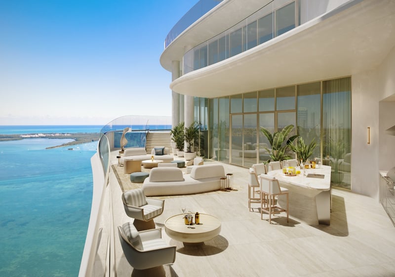 Curved waterfront penthouse terrace with outdoor lounge seating, dining island, summer kitchen, floor-to-ceiling glass, and expansive bay views at St Regis Residences Miami in Brickell, showcasing ultra luxury and exclusive living.