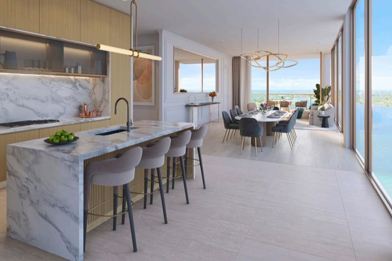 Open chef kitchen with a waterfall marble island, dining area, and water views at The Berkeley in West Palm Beach, showcasing luxury and ultra luxury condos with seamless entertaining space.