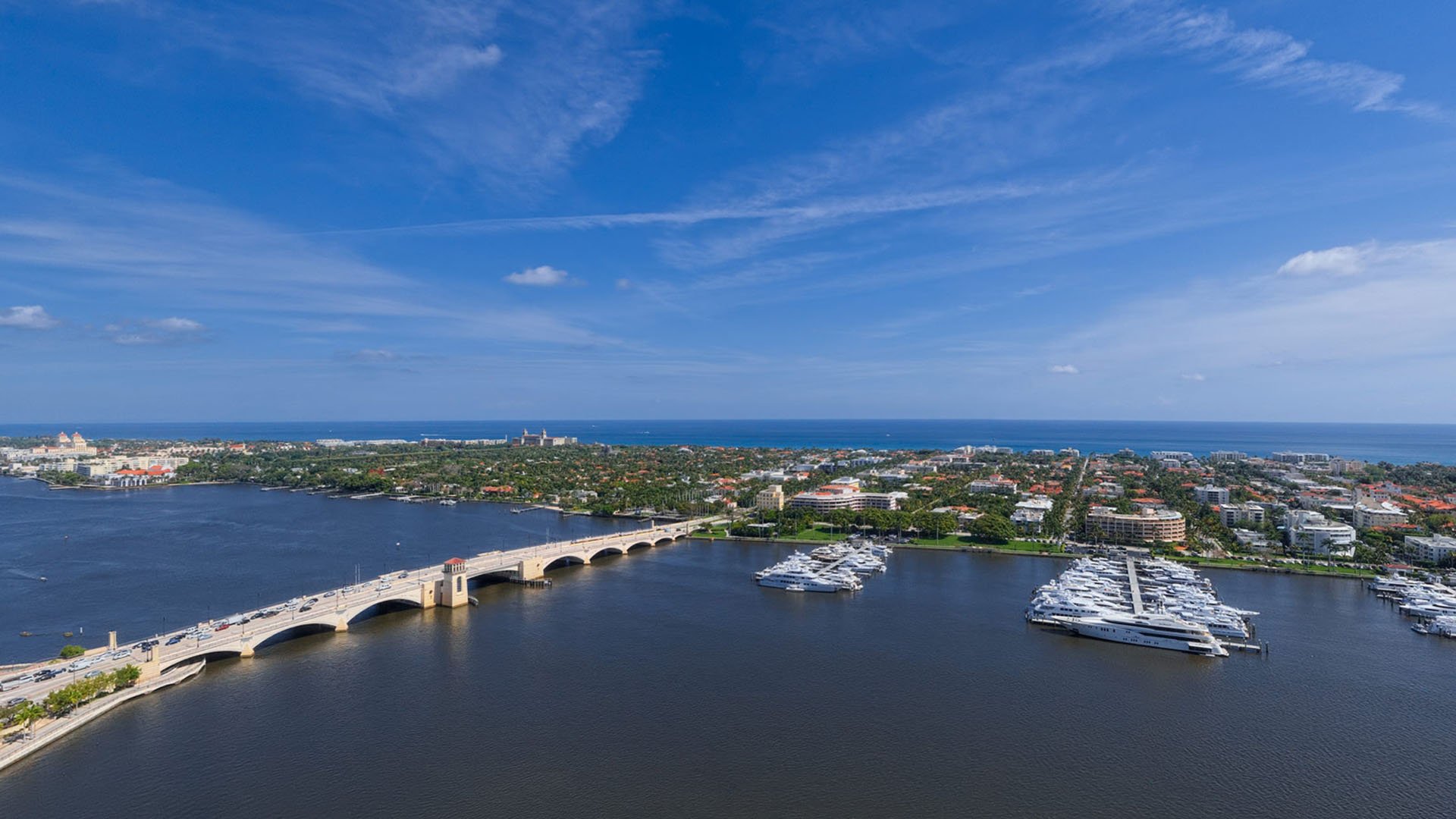 Aerial view of a bridge, yacht marina, and waterfront neighborhood near The Bristol Palm Beach in Palm Beach, showcasing luxury and ultra luxury condos with expansive water and skyline vistas.