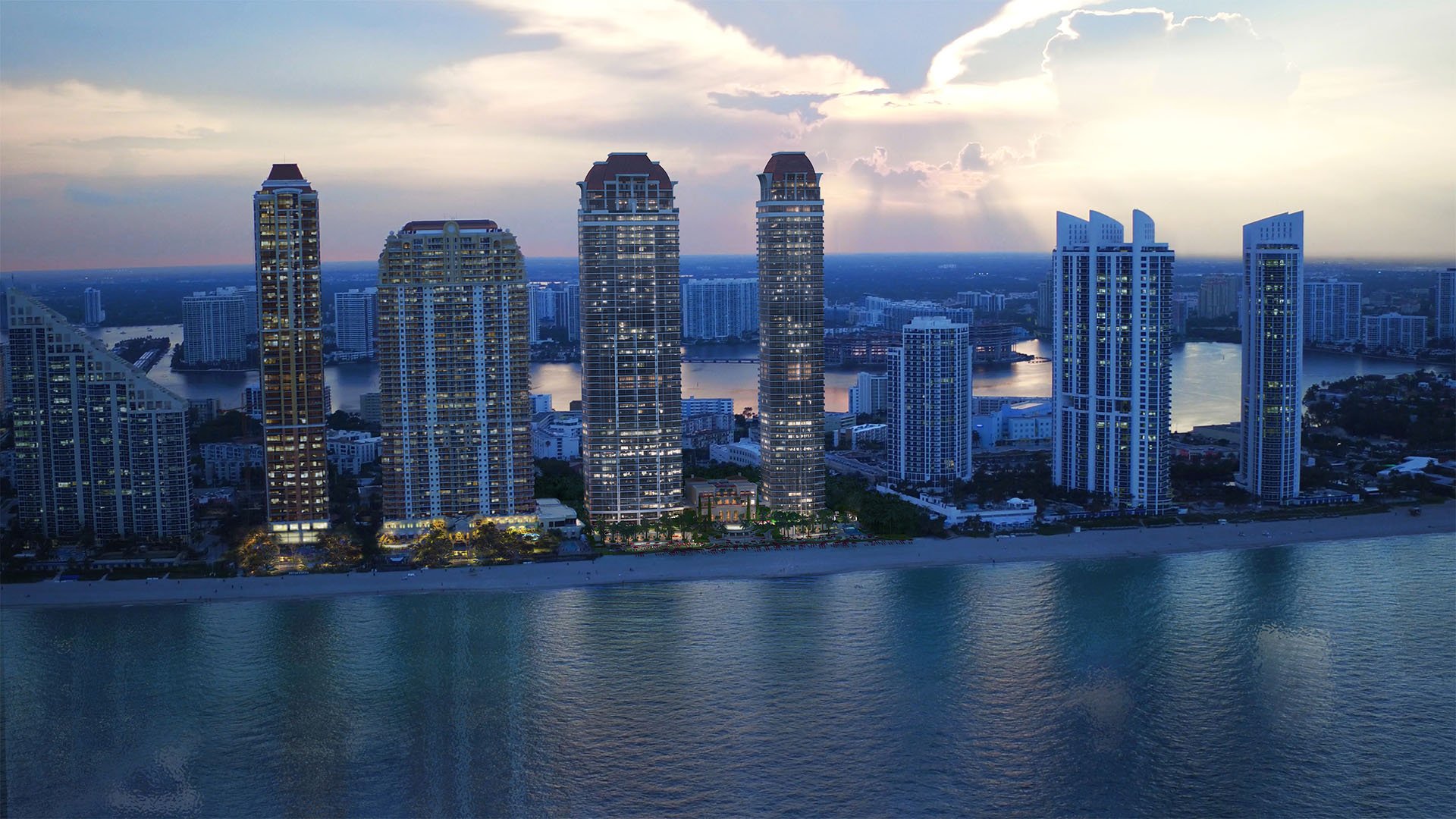Dusk waterfront skyline with illuminated towers reflected over the bay at The Estates at Acqualina, Sunny Isles Beach, a community of luxury and ultra luxury condos.