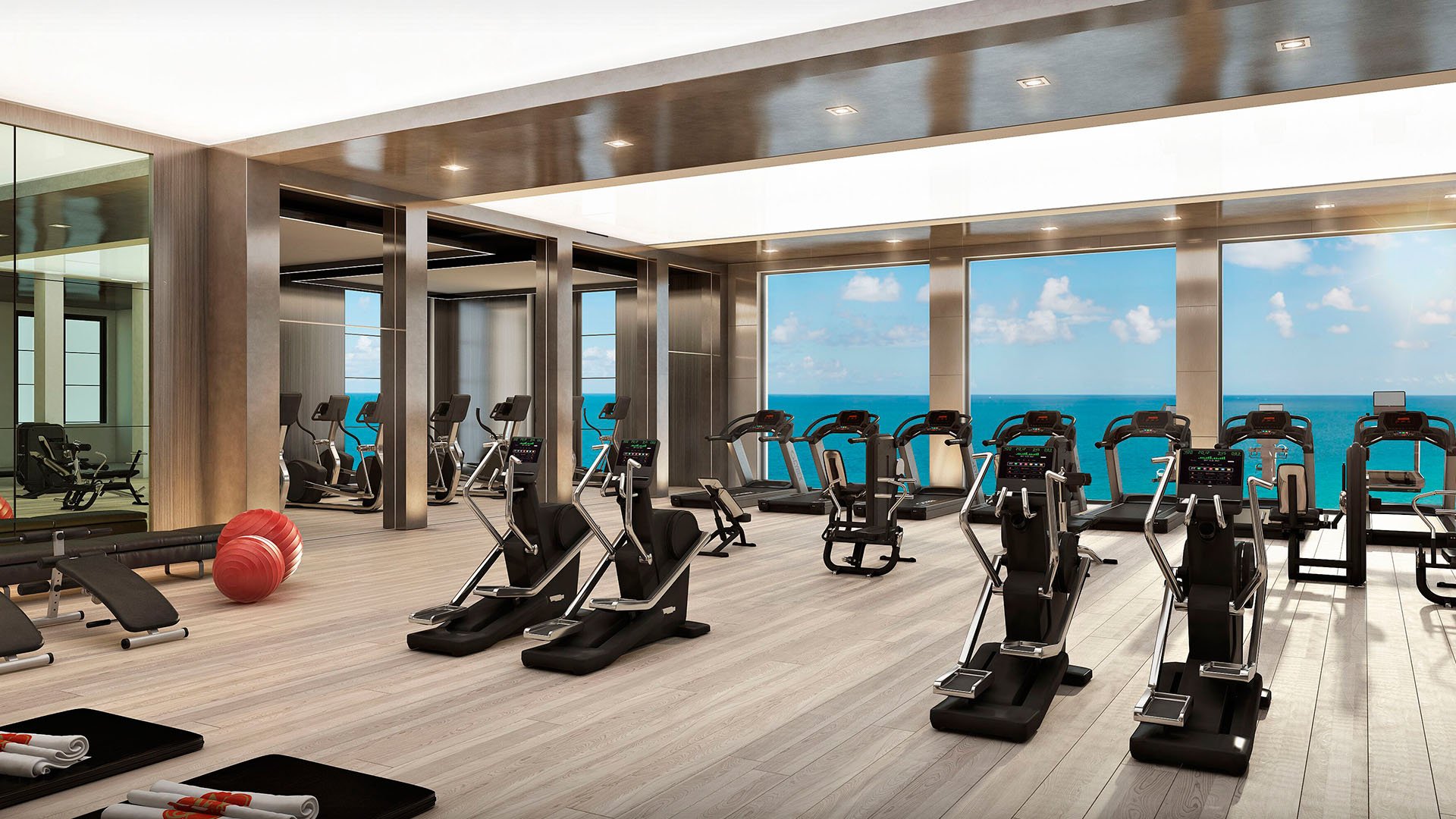 Ocean-view fitness center with treadmills, strength equipment, and full-height windows at The Estates at Acqualina, Sunny Isles Beach, a community of luxury and ultra luxury condos.