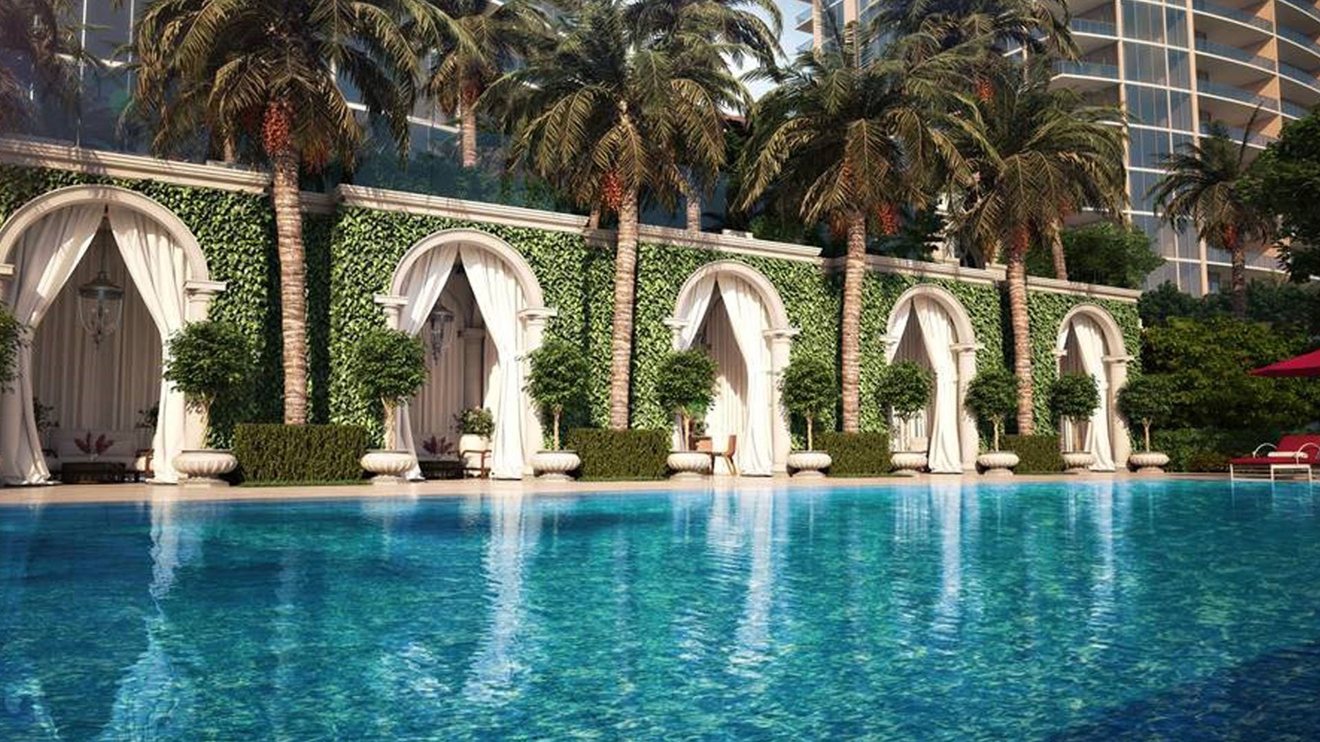 Poolside cabanas framed by arches, palms, and reflective water at The Estates at Acqualina, Sunny Isles Beach, a community of luxury and ultra luxury condos.