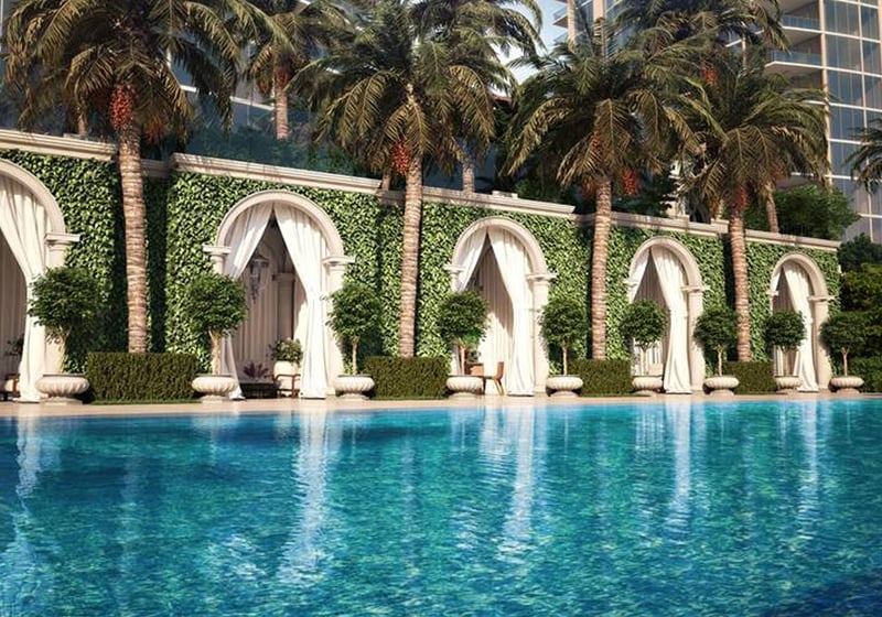 Poolside cabanas framed by arches, palms, and reflective water at The Estates at Acqualina, Sunny Isles Beach, a community of luxury and ultra luxury condos.
