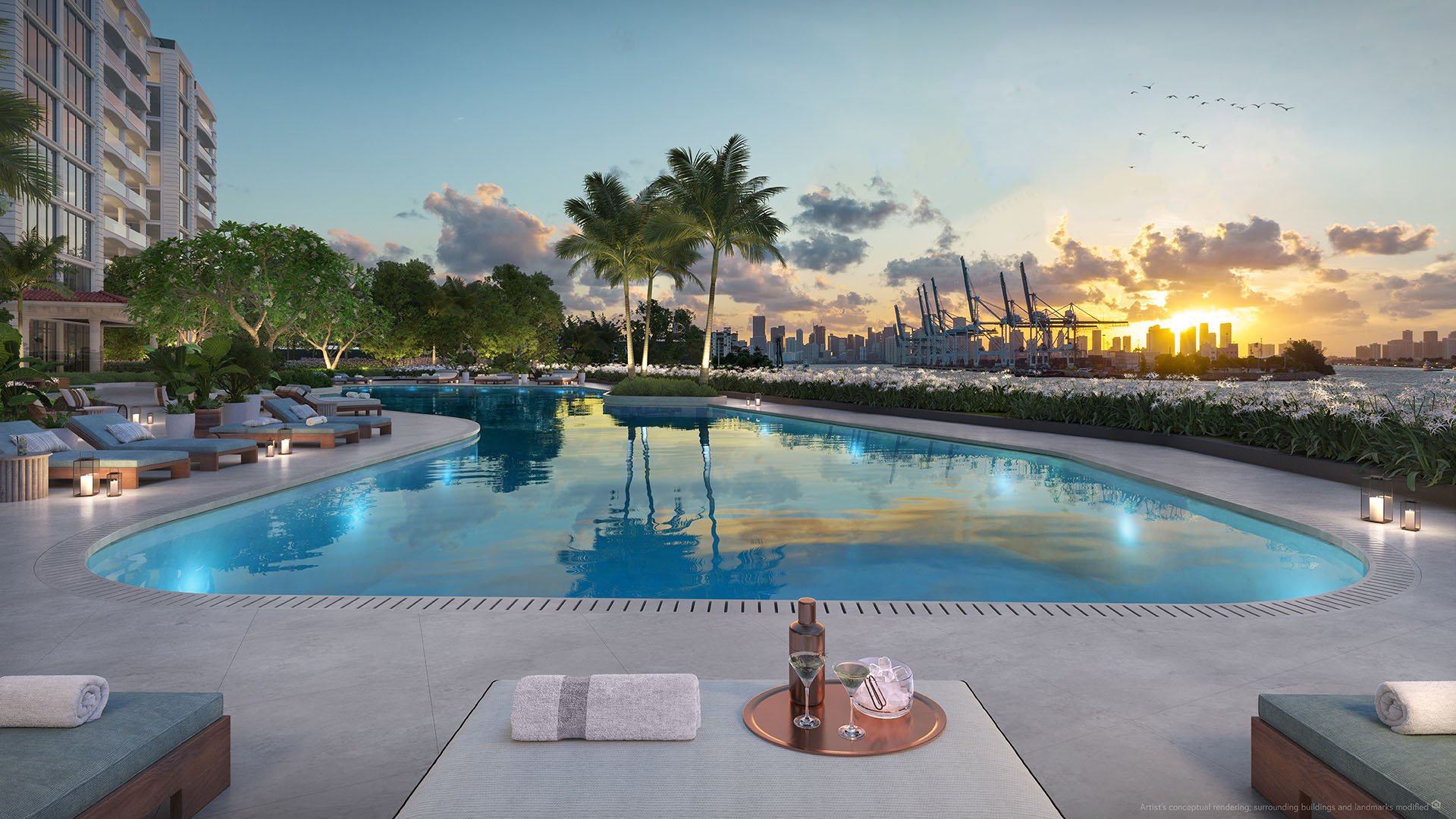Bayfront infinity pool at The Residences at Six Fisher Island, Fisher Island Miami Beach, Florida, sunset west view toward downtown Miami and PortMiami cranes, showcasing luxury and ultra luxury preconstruction condos amenities.