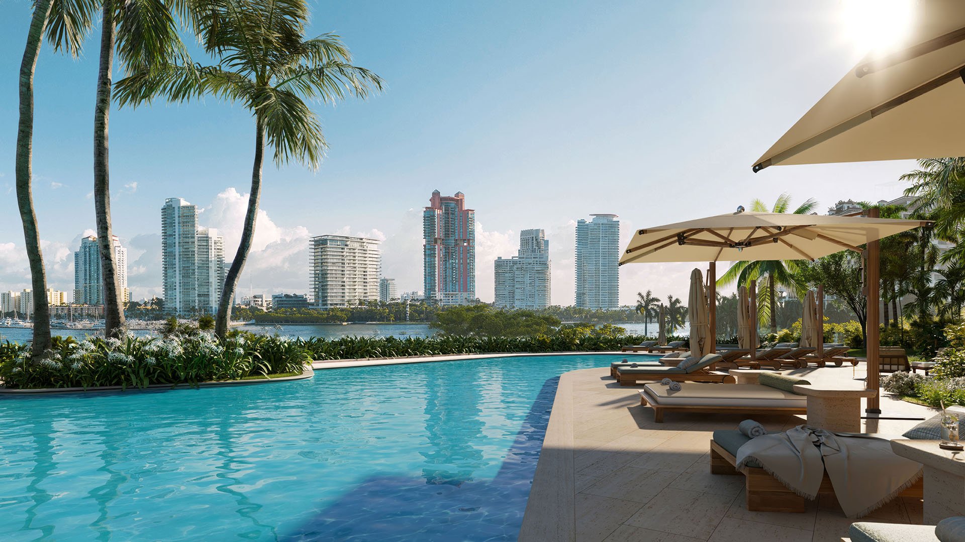 Resort pool deck at The Residences at Six Fisher Island, Fisher Island Miami Beach, Florida, east-facing Biscayne Bay views and Miami skyline backdrop with loungers and umbrellas, for luxury and ultra luxury preconstruction condos.