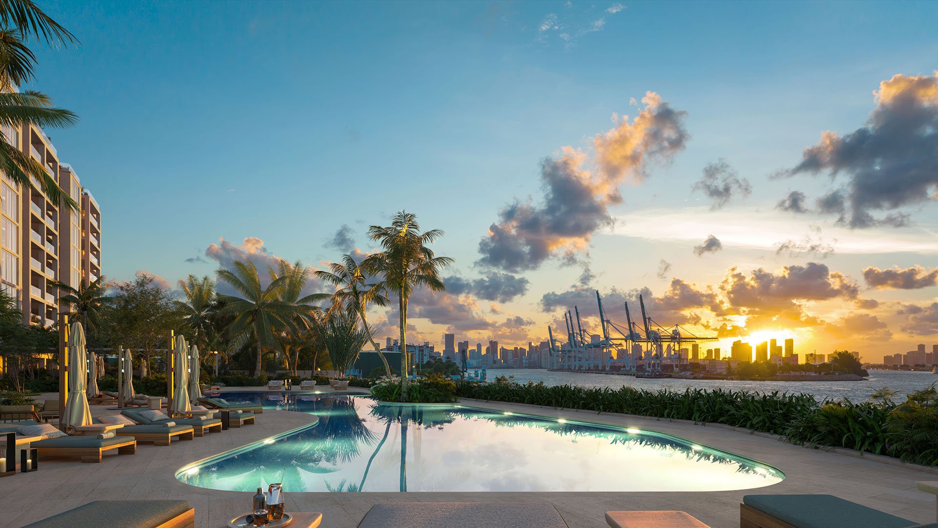 Sunset lounge deck and bayfront pool at The Residences at Six Fisher Island, Fisher Island Miami Beach, Florida, with palm trees and PortMiami crane views, highlighting luxury and ultra luxury preconstruction condos lifestyle.
