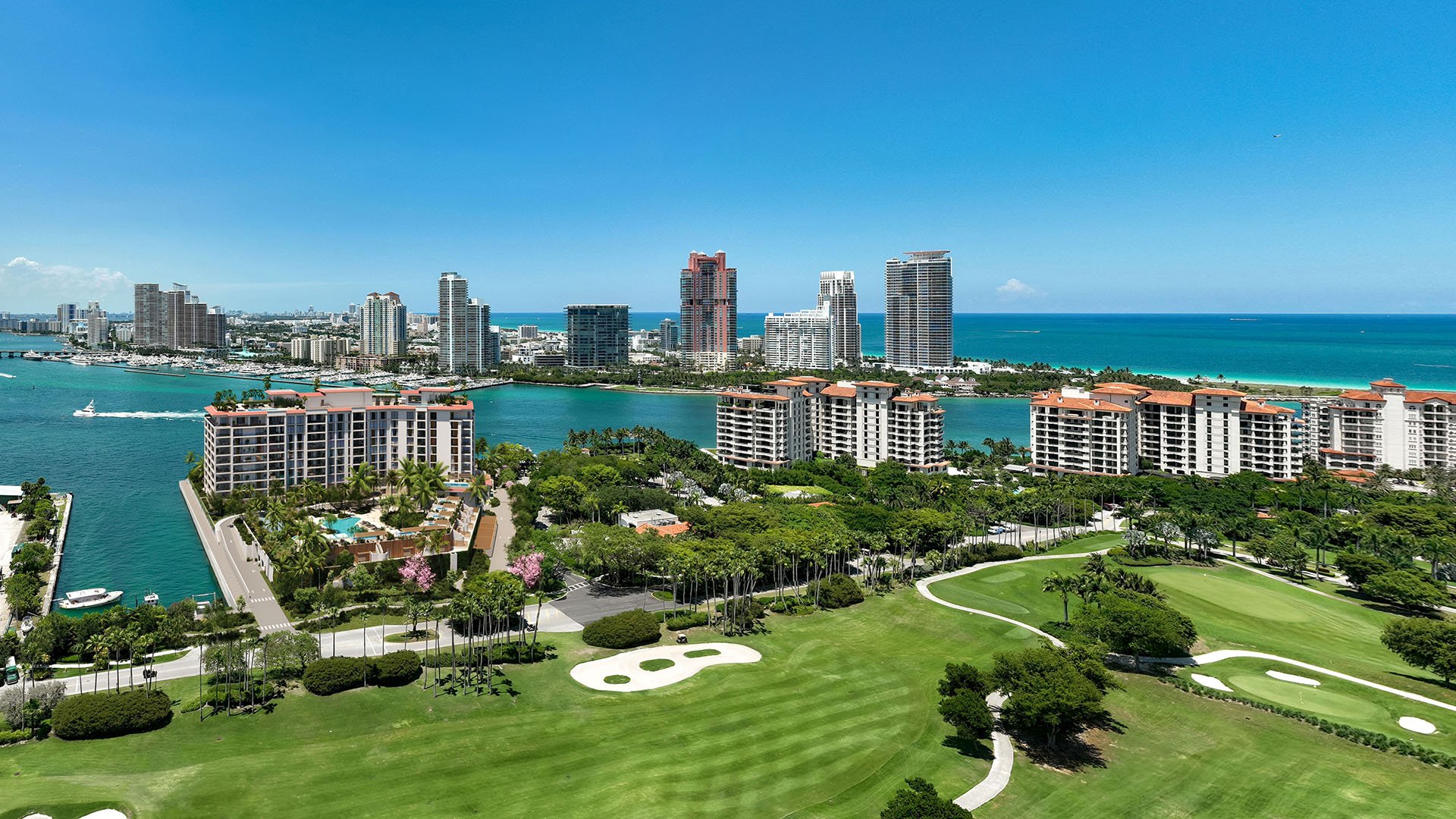 Aerial of Fisher Island golf course near The Residences at Six Fisher Island, Fisher Island, Miami Beach, Florida, with Biscayne Bay, Miami Beach skyline and Atlantic Ocean beyond, reinforcing luxury and ultra luxury preconstruction condos lifestyle.