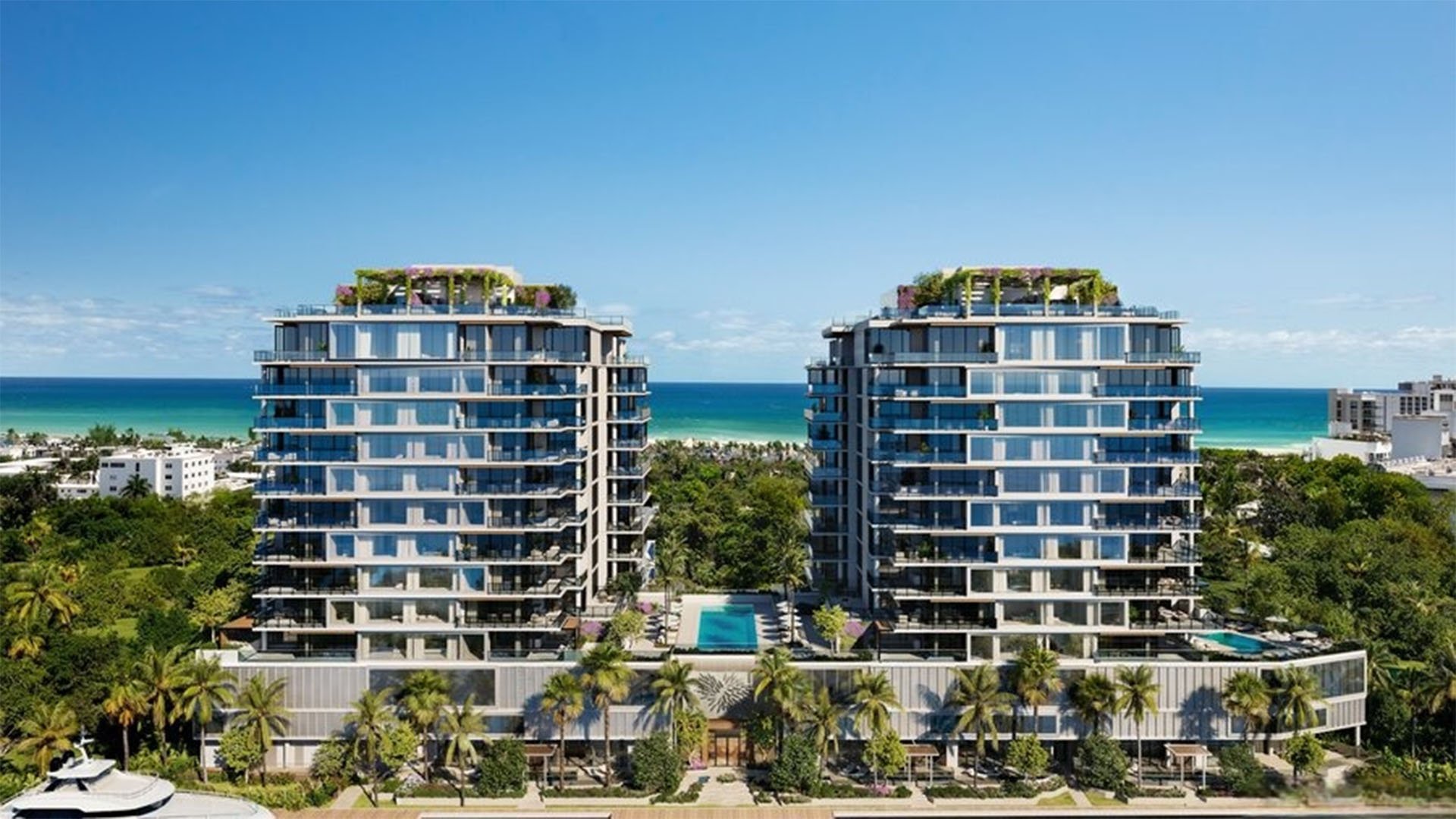 Aerial view of twin ocean-view towers at The Ritz-Carlton Residences, Fort Lauderdale, showing luxury and ultra luxury condos, palm-lined grounds, a central pool, and the ocean beyond.
