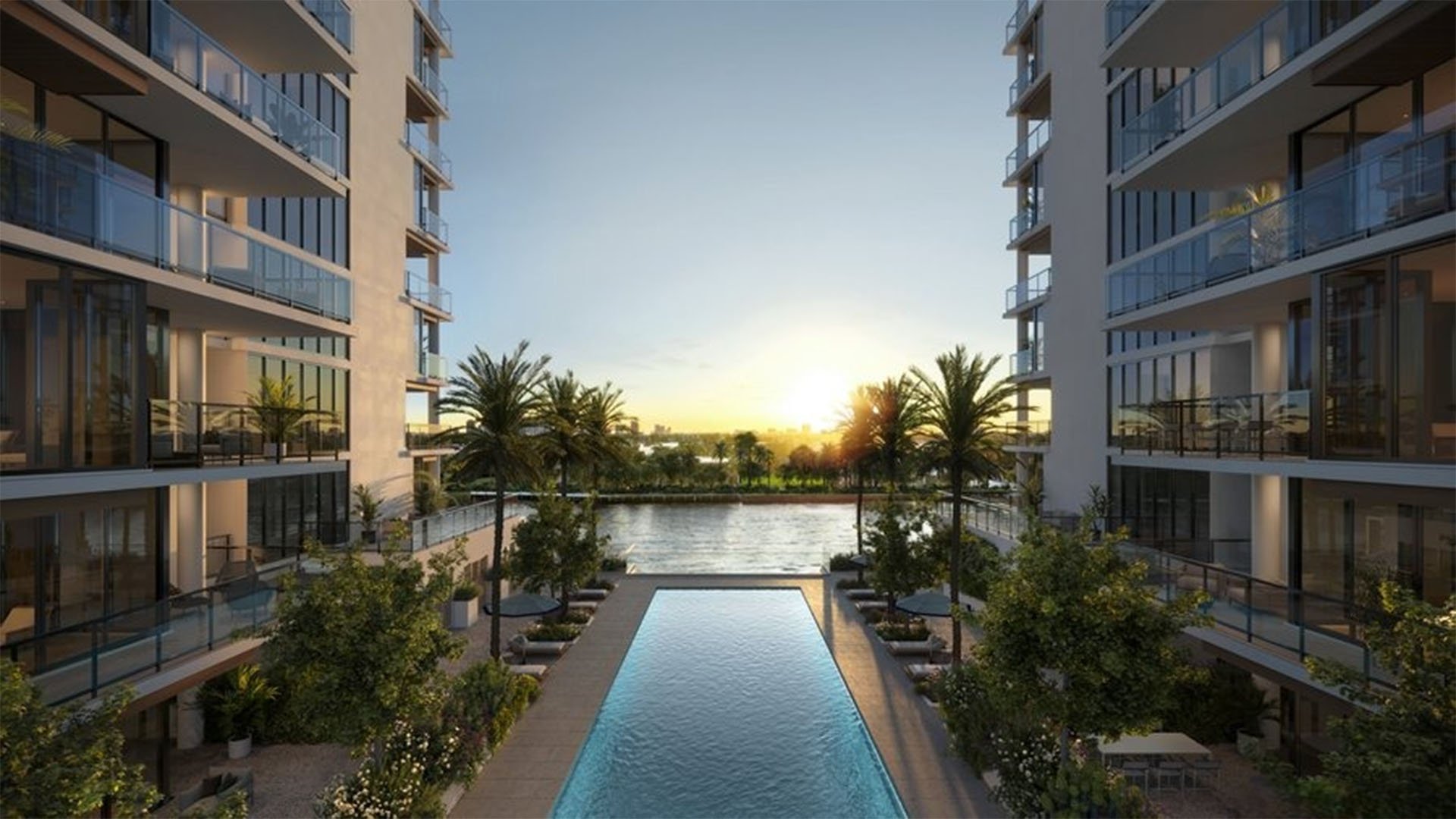 Courtyard lap pool at The Ritz-Carlton Residences, Fort Lauderdale, between twin towers of luxury and ultra luxury condos, with palm trees, loungers, glass balconies, and a water view at dusk.
