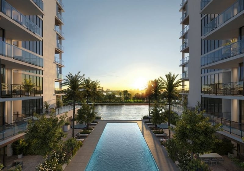 Courtyard lap pool at The Ritz-Carlton Residences, Fort Lauderdale, between twin towers of luxury and ultra luxury condos, with palm trees, loungers, glass balconies, and a water view at dusk.