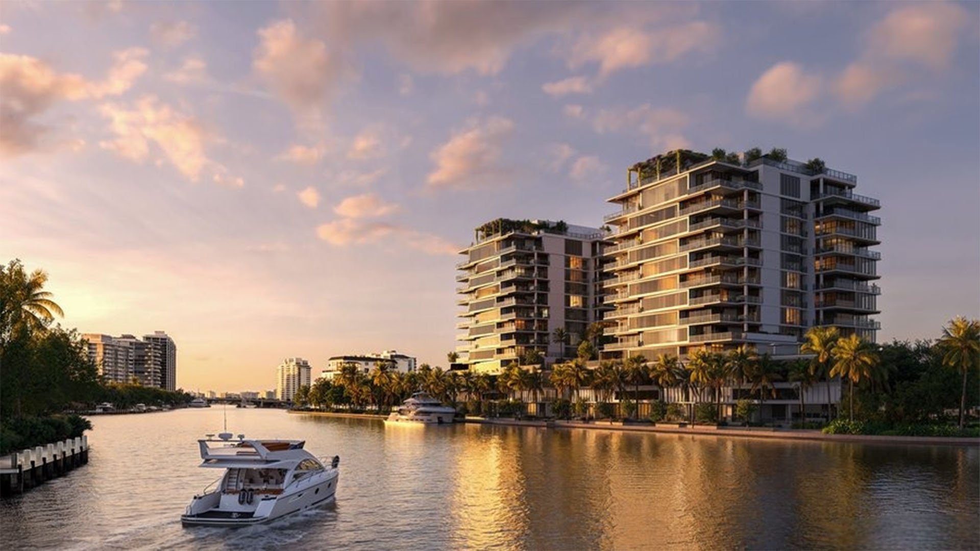 Waterfront view of The Ritz-Carlton Residences, Fort Lauderdale, with luxury and ultra luxury condos rising beside a calm channel, palm-lined shoreline, and a yacht cruising past at sunset.