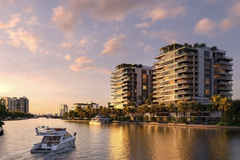 Waterfront view of The Ritz-Carlton Residences, Fort Lauderdale, with luxury and ultra luxury condos rising beside a calm channel, palm-lined shoreline, and a yacht cruising past at sunset.