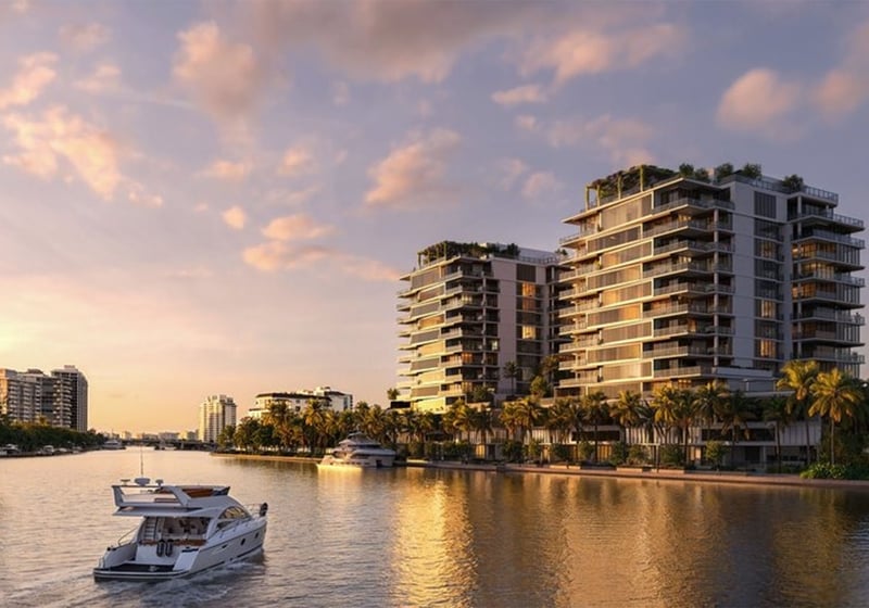 Waterfront view of The Ritz-Carlton Residences, Fort Lauderdale, with luxury and ultra luxury condos rising beside a calm channel, palm-lined shoreline, and a yacht cruising past at sunset.