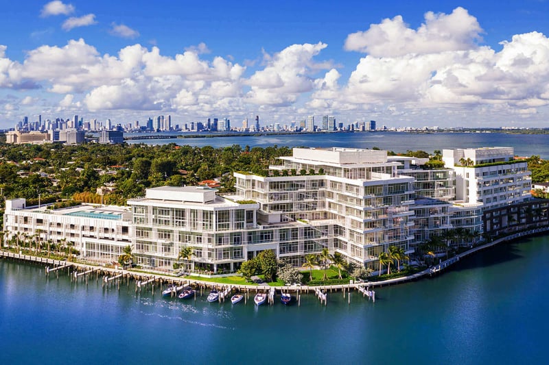 Aerial waterfront overview with marina slips and a distant skyline at The Ritz-Carlton Residences Miami Beach in Miami Beach, presenting luxury and ultra luxury condos on a broad bayfront site.