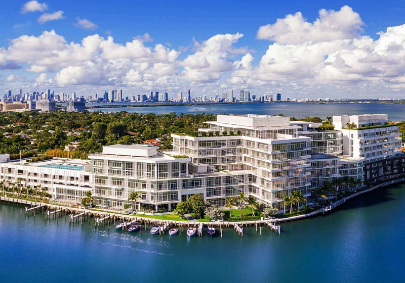 Aerial waterfront overview with marina slips and a distant skyline at The Ritz-Carlton Residences Miami Beach in Miami Beach, presenting luxury and ultra luxury condos on a broad bayfront site.