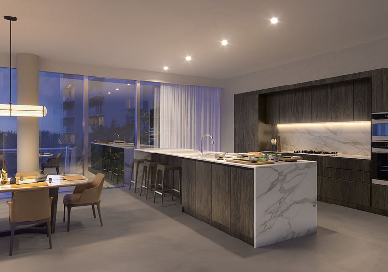 Evening view of Marina Tower Residence 01 kitchen and dining at The Ritz-Carlton Residences Pompano Beach, Florida, featuring marble waterfall island and designer lighting, showcasing luxury and ultra luxury preconstruction condos interiors.
