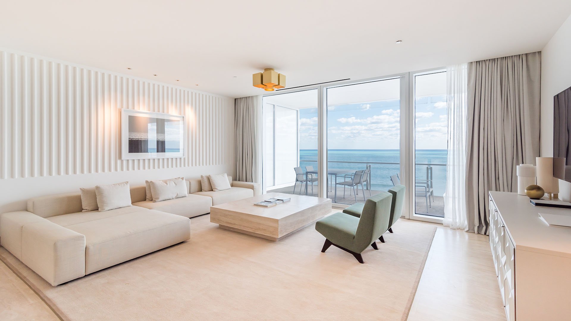 Beachfront living room with a white sectional and sliding glass wall opening to an ocean-view terrace at The Surf Club Four Seasons, Fort Lauderdale luxury and ultra luxury condos.