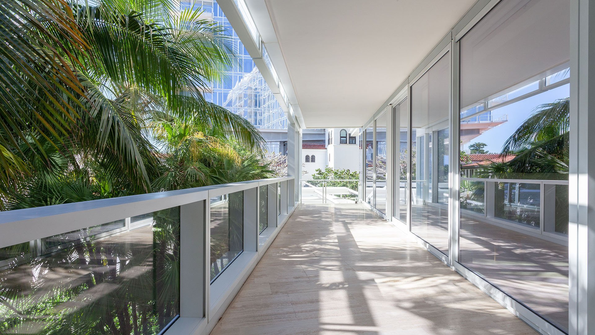 Covered terrace gallery with glass walls, palm views, and a long shaded walkway at The Surf Club Four Seasons, Fort Lauderdale luxury and ultra luxury condos.