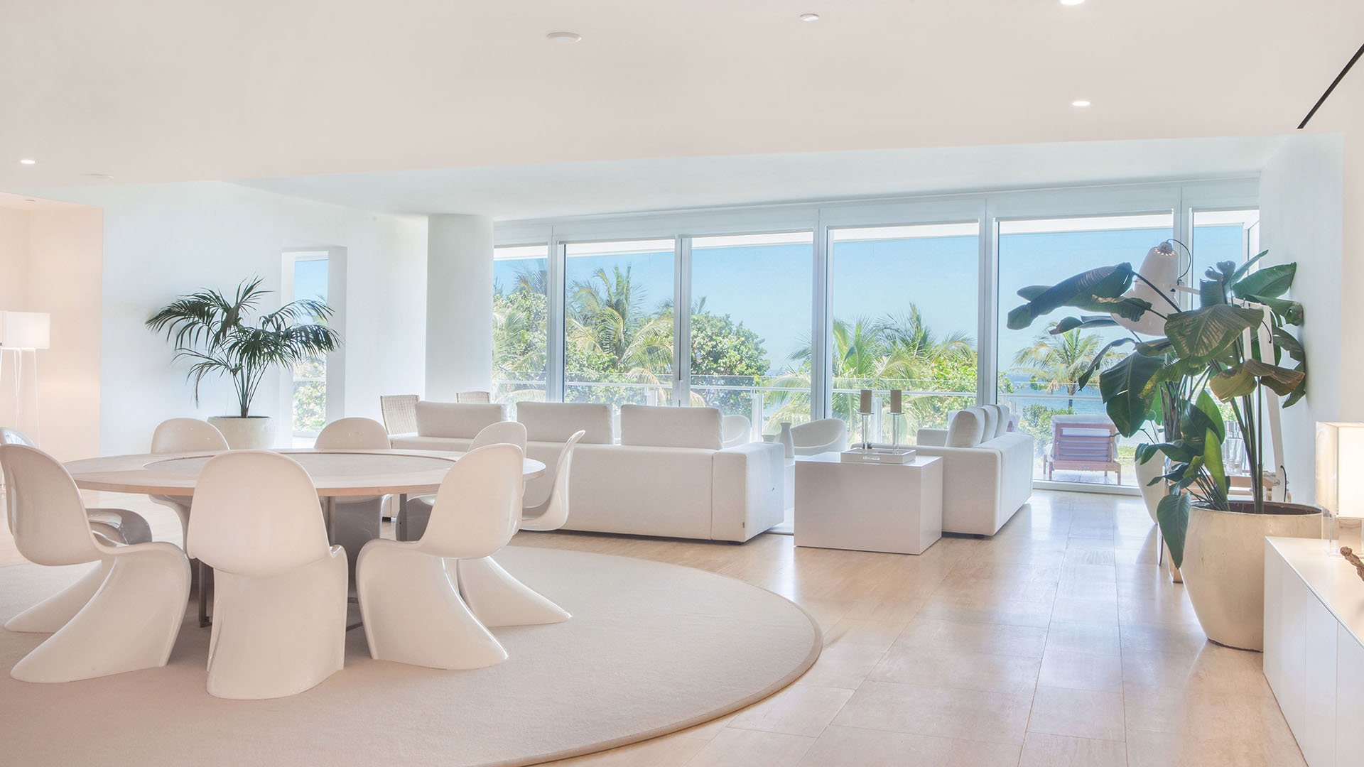 Great room with round dining table, lounge seating, and broad windows looking over palm landscaping at The Surf Club Four Seasons, Fort Lauderdale luxury and ultra luxury condos.