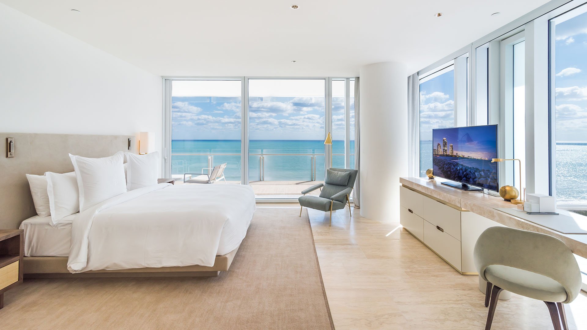 Oceanfront primary bedroom with desk, media console, and a full wall of windows framing the water at The Surf Club Four Seasons, Fort Lauderdale luxury and ultra luxury condos.