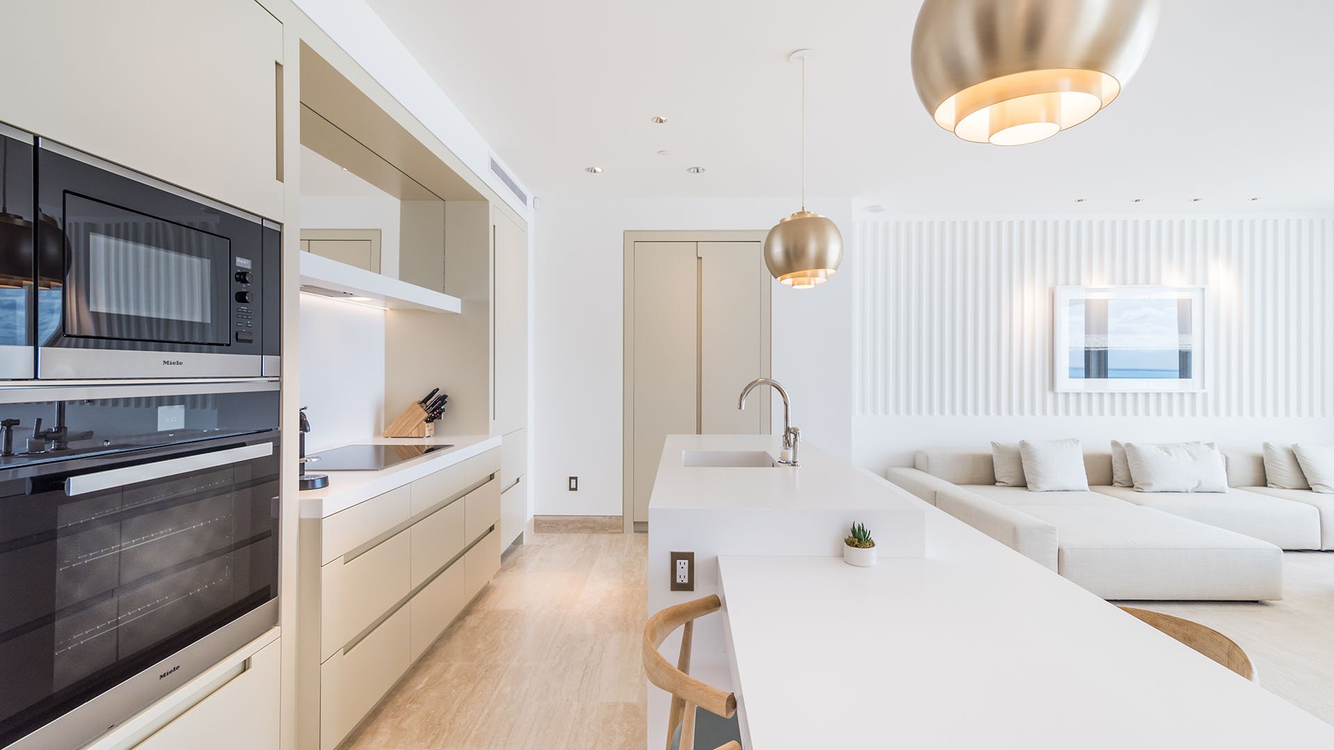 Open-concept white chef kitchen with a long island, built-in ovens, and lounge seating at The Surf Club Four Seasons, Fort Lauderdale luxury and ultra luxury condos.