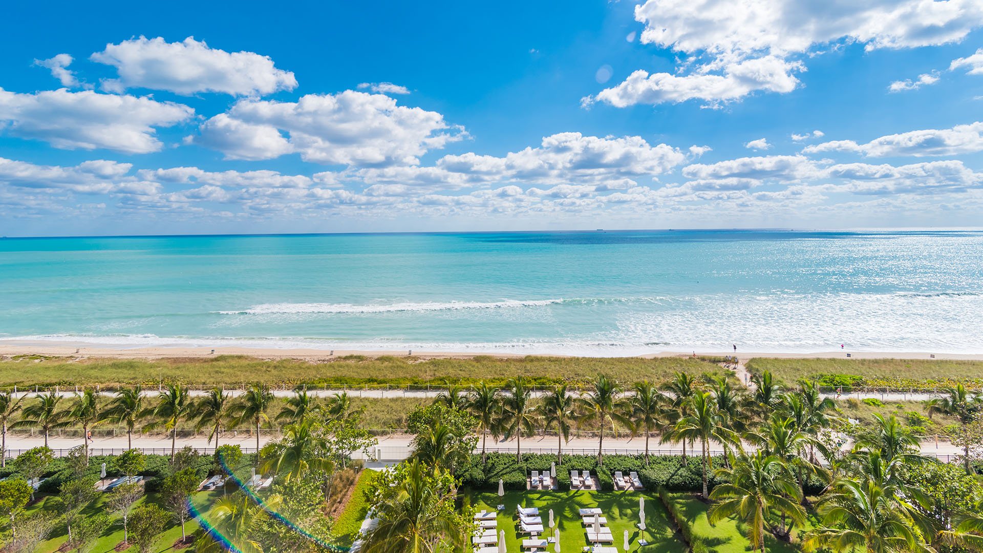 Panoramic oceanfront lawn and beach view with palms, lounge seating, and a bright horizon at The Surf Club Four Seasons, Fort Lauderdale luxury and ultra luxury condos.