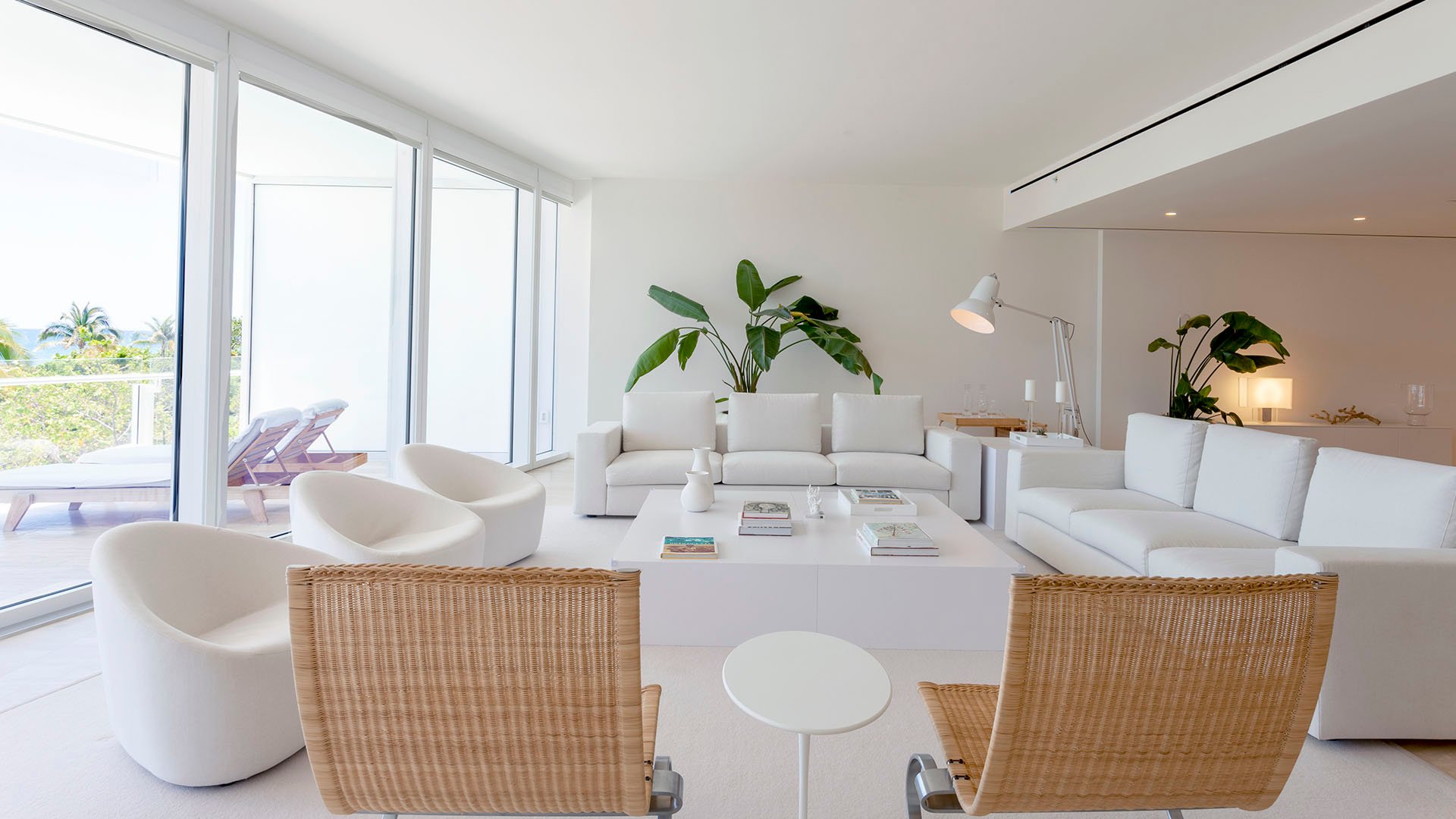 Sunlit living room with woven accent chairs, white seating, and a terrace just beyond the glass at The Surf Club Four Seasons, Fort Lauderdale luxury and ultra luxury condos.