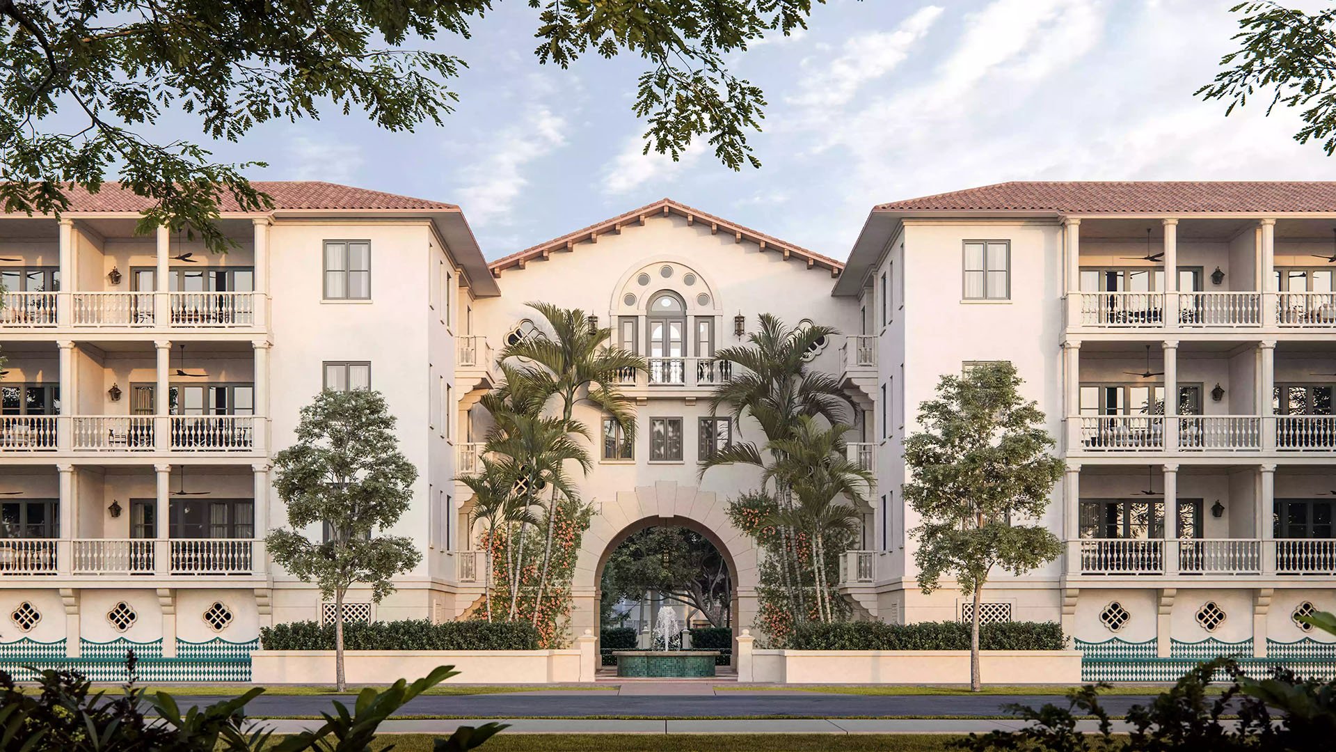 The Village at Coral Gables exterior in Coral Gables, Miami showing Spanish Mediterranean residences with central archway and courtyard fountain framed by palm trees; luxury and ultra luxury preconstruction condos community.