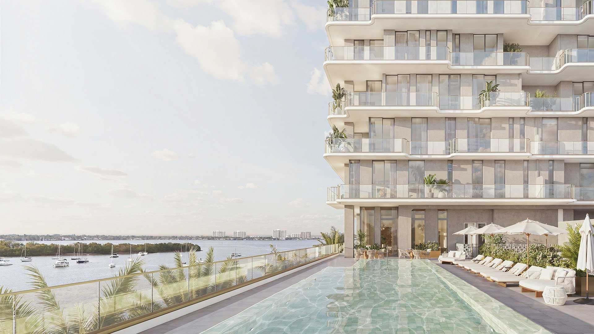 Bayfront pool deck lined with loungers beside the tower facade at Tula Residences in North Bay Village, presenting luxury and ultra luxury condos with resort-style waterfront amenities and contemporary architectural lines.
