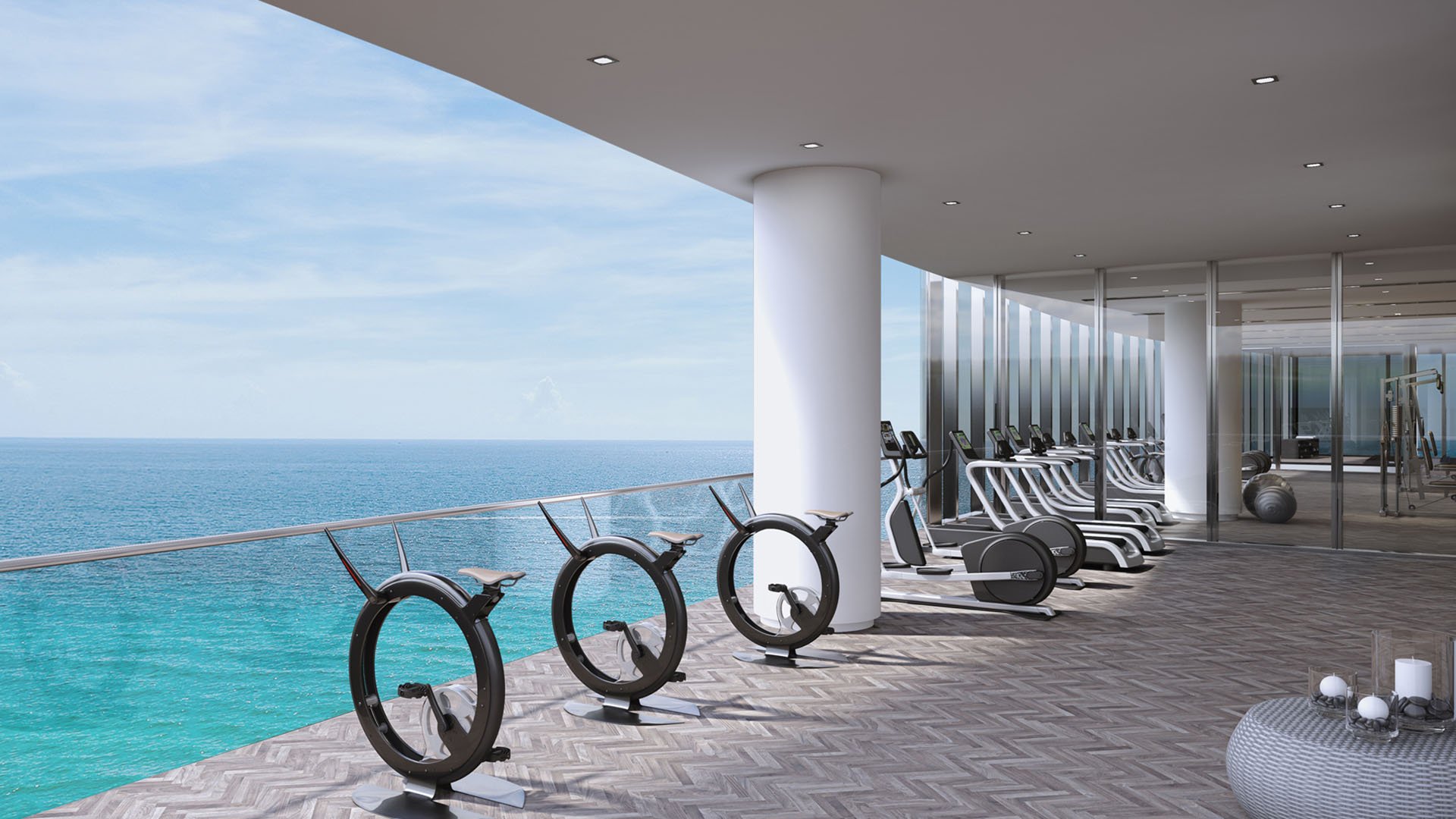 Turnberry Ocean Club in Sunny Isles Beach luxury and ultra luxury condos showcase an outdoor fitness terrace with stationary bikes, lounge seating, and open ocean views.