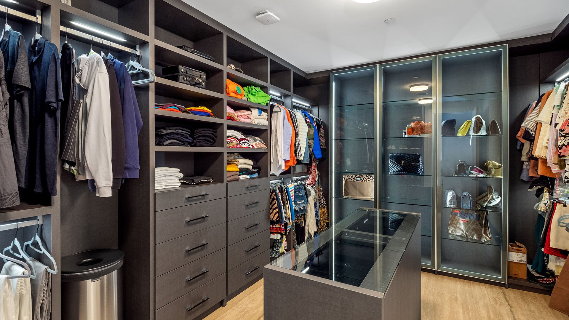 Turnberry Ocean Club in Sunny Isles Beach luxury and ultra luxury condos showcase a walk-in closet with center island storage, glass display cabinets, and custom shelving.