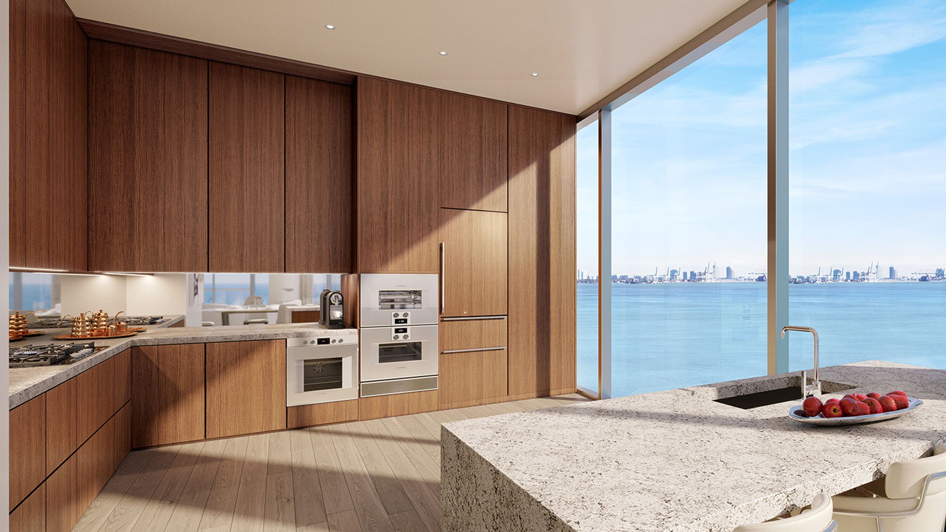 Una Residences Brickell, Miami gourmet kitchen with warm wood cabinetry, built-in appliances and stone waterfall island beside floor-to-ceiling windows, featuring Biscayne Bay views in luxury and ultra luxury preconstruction condos.