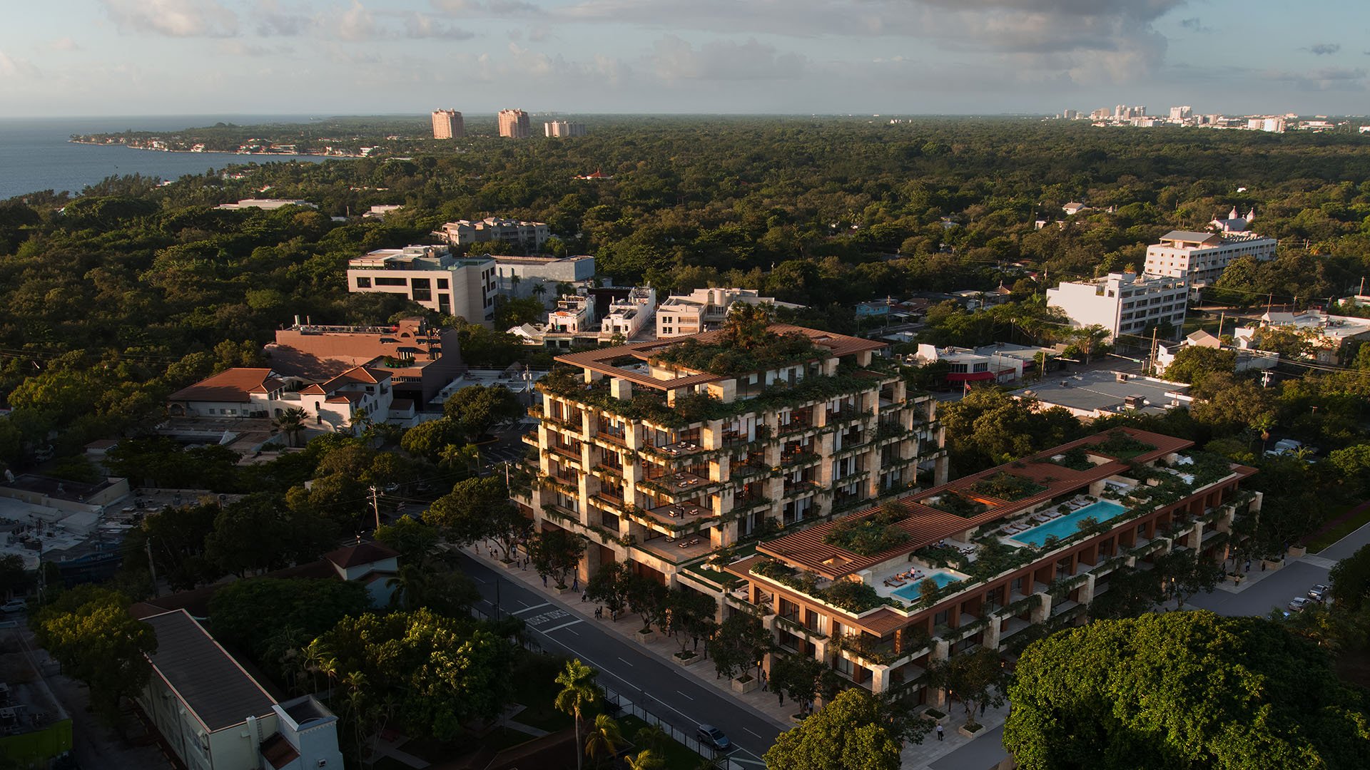Aerial sunset view of Ziggurat in Coconut Grove, Miami, Florida, with lush green terraces and a rooftop pool, showcasing luxury amenities and ultra luxury preconstruction condos near Biscayne Bay.