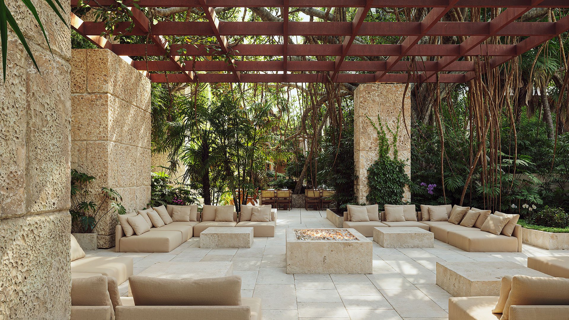 Pergola-covered courtyard lounge with fire pit and sectional seating at Ziggurat Coconut Grove, Miami, Florida, surrounded by tropical gardens, representing luxury social spaces and ultra luxury preconstruction condos.