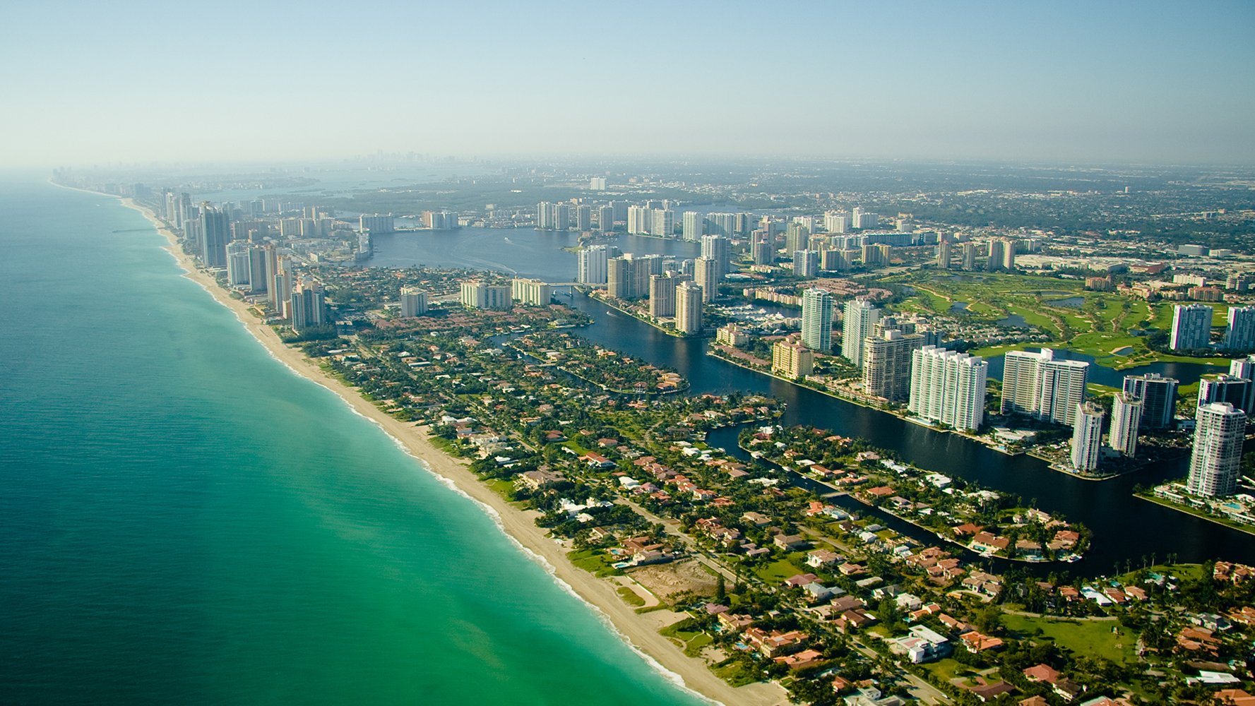 Aerial view of a long coastline with beaches, high-rise buildings, and water canals in a densely populated city.