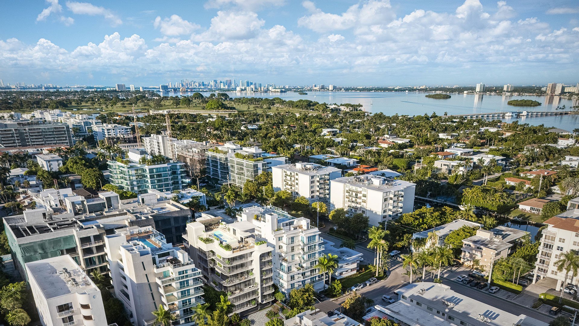 Aerial neighborhood view around Alma Bay Harbor in Bay Harbor Islands, Miami, with Biscayne Bay and a distant skyline, highlighting luxury and ultra luxury preconstruction condos in a peaceful waterfront enclave.