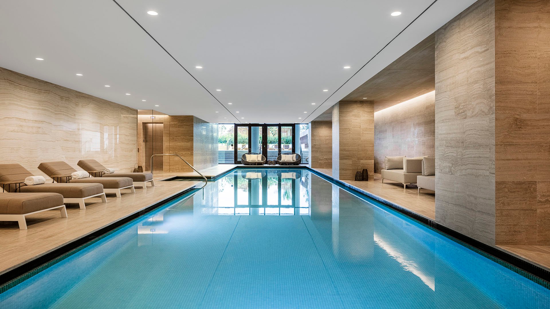 Long indoor pool view at Arte Surfside, Surfside, Florida, highlighting luxury and ultra luxury condos with a spa-like lap pool, warm lighting, and lounge seating.