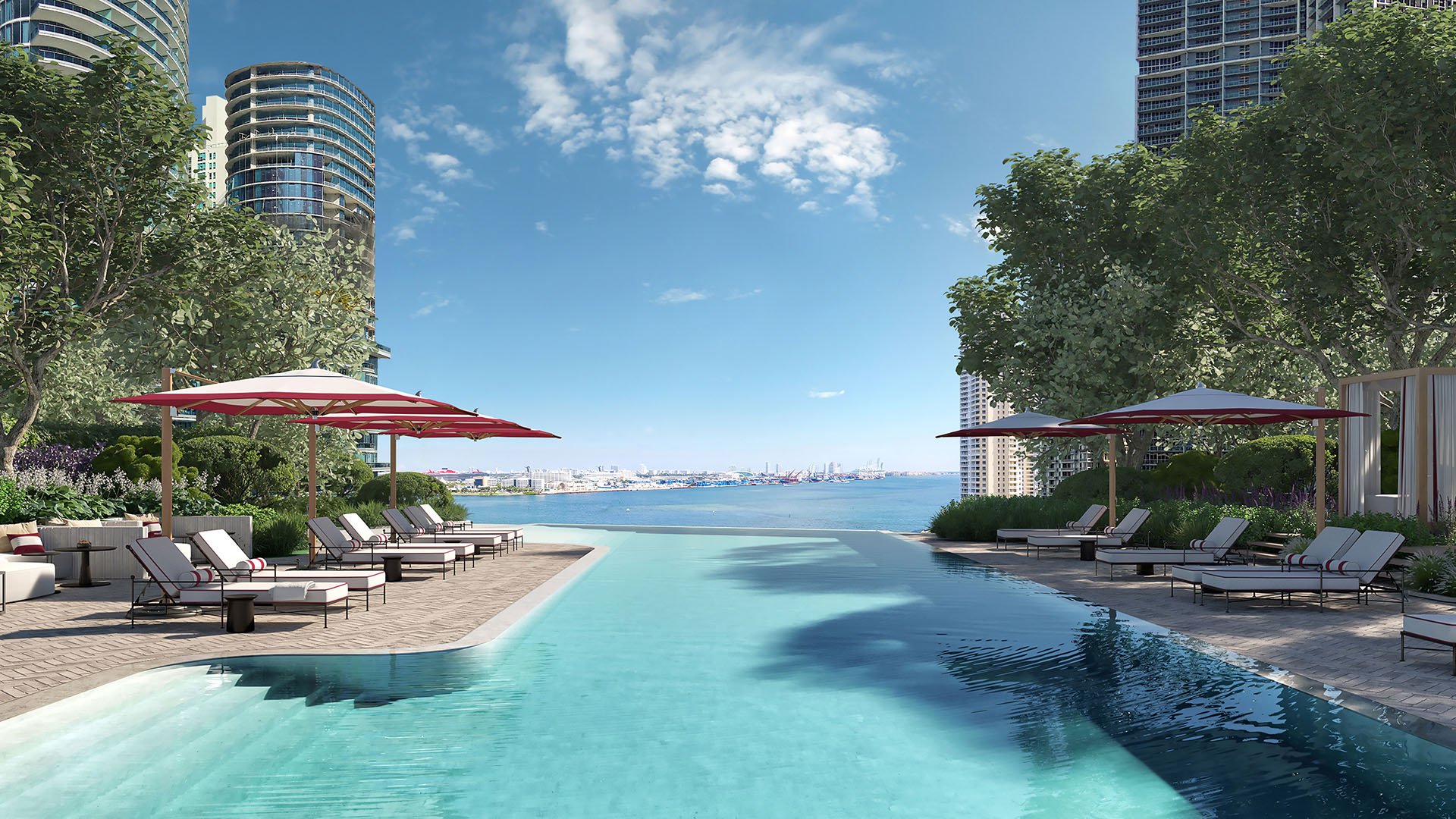 Baccarat Residences in Brickell, Miami, luxury and ultra luxury condos featuring a waterfront pool terrace, red umbrellas, sun loungers, landscaped edges, and open bay views.